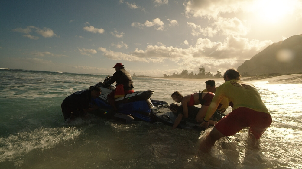 A sunset scene captures the "Rescue: HI-Surf" cast members at work in the waves, backlit by golden sunlight against a backdrop of mountains.