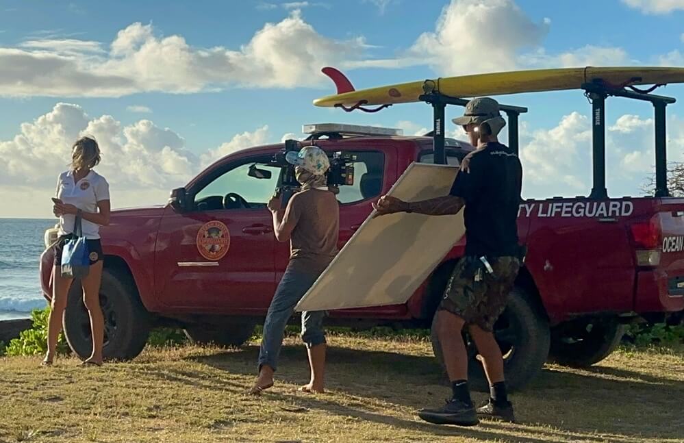 Cinematographer Anka Malatynska captures a handheld shot from beside a red lifeguard truck with surfboards mounted on top during golden hour by the ocean