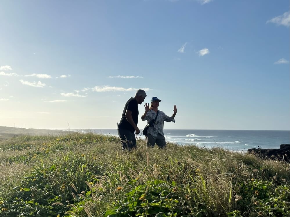 Cinematographer Anka Malatynska finds the frame from a grassy coastal hilltop, with ocean waves in the background under a bright blue sky