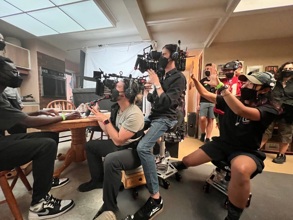 Cinematographer Rina Yang, BSC directs the camera from behind a wooden table alongside fellow camera operators and crew members.