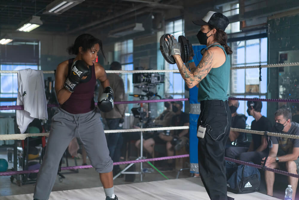 Actor Ryan Destiny practices fight choreography with director Rachel Morrison, ASC holding focus mitts in a boxing ring, with film crew visible in the background.