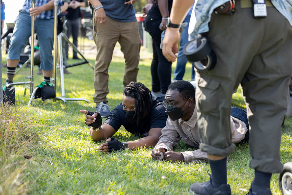 Cinematographer Jomo Fray lies on the grass beside actor Ethan Herisse while pointing out a low-angle shot