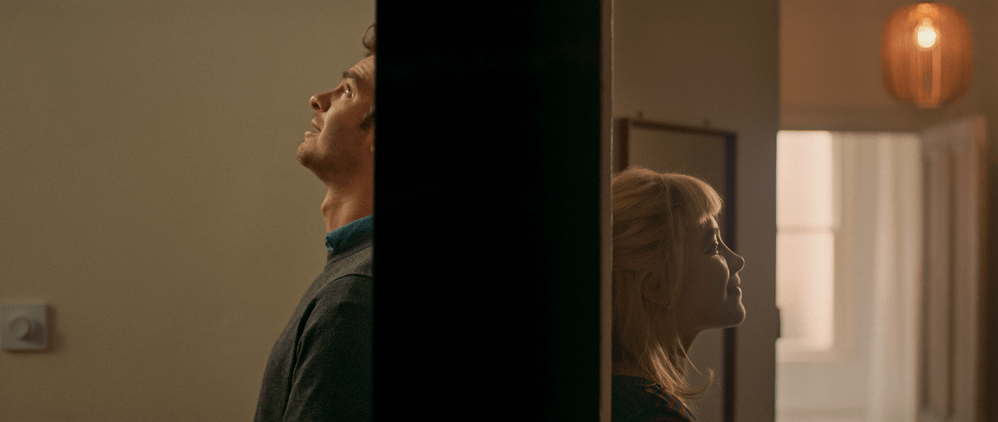 A split-screen amber lit composition showing Alumt (Florence Pugh) and Tobias (Andrew Garfield) on opposite sides of the divide looking upward with contemplative expressions in the feature “We Live In Time”